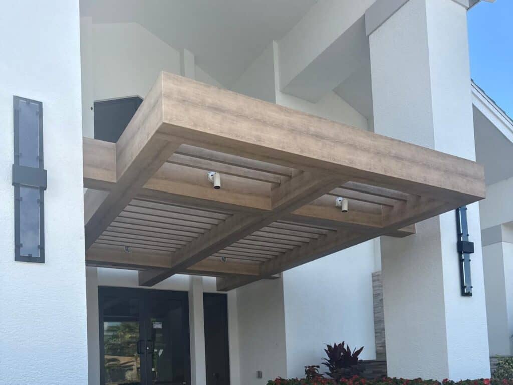 Finished custom welded aluminum entry canopy with wood-look slat underside and integrated lighting on a commercial building in Fort Myers Florida