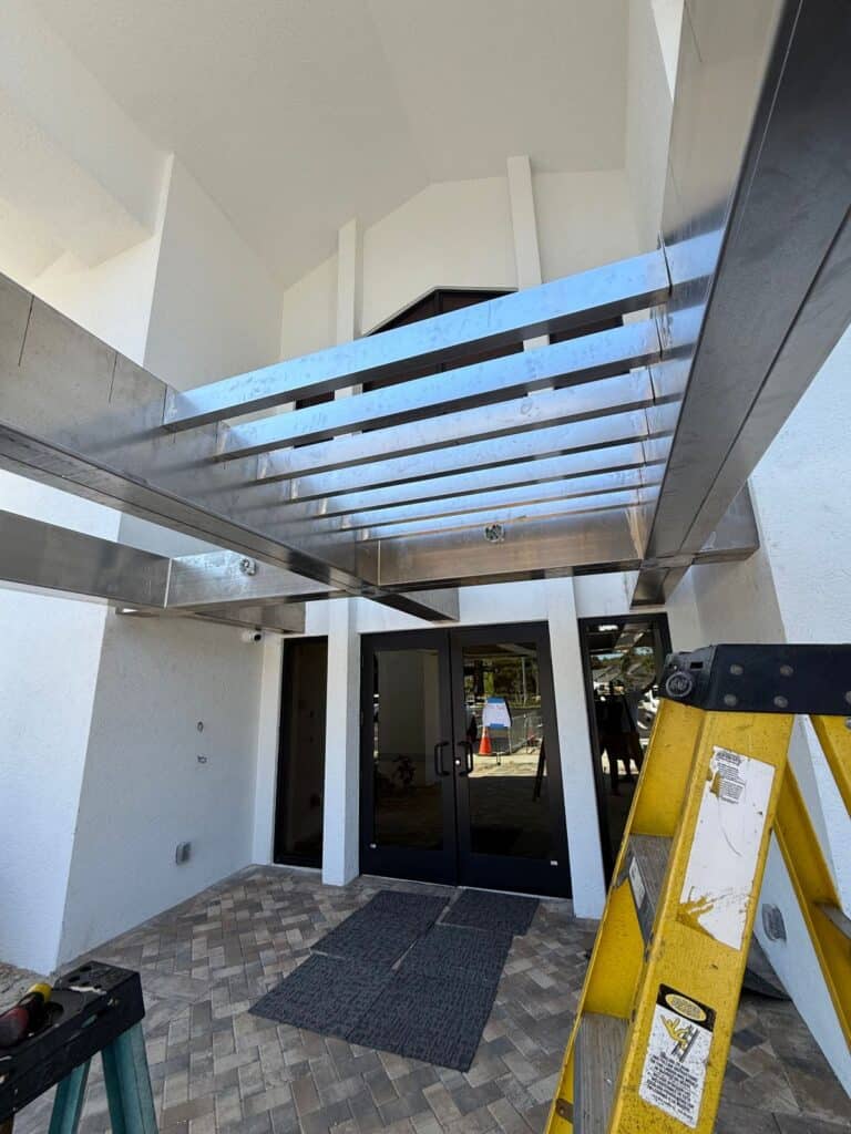 Installed structural welded aluminum canopy underside with integrated aluminum slats over a commercial building entryway in Florida