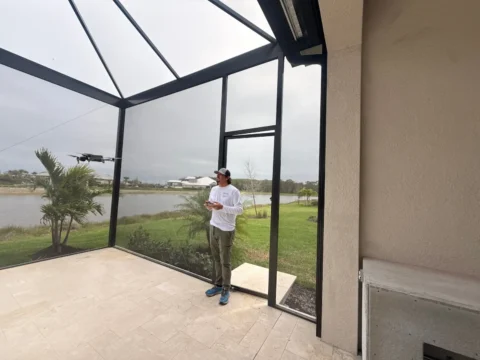 Man standing inside a new pool enclosure in Naples near a screen door with bronze aluminum framing and lake view.