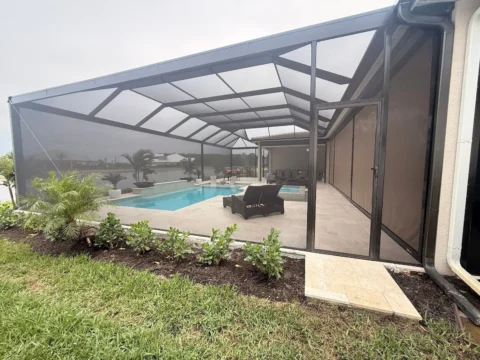 Exterior entry view of a new pool enclosure with bronze aluminum frame, screened walls, door, and pool area in Naples.