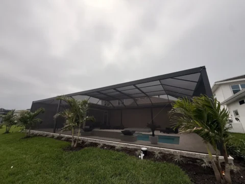 Full exterior view of a new pool enclosure with bronze aluminum framing and screened walls behind a landscaped yard in Naples.