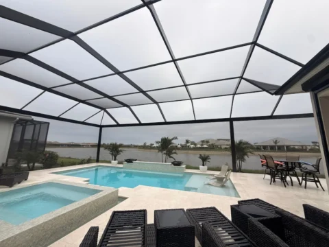 New pool enclosure in Naples with bronze aluminum framing, open picture-window view, pool, spa, and lake in the background.