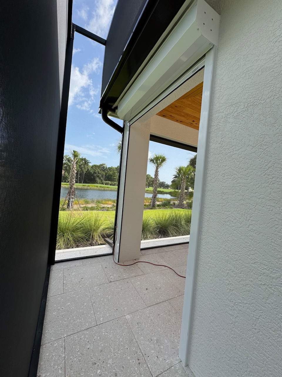 Close-up of a roll-down hurricane shutter housing partially retracted, with a golf course pond view through the pool cage — SAS Aluminum