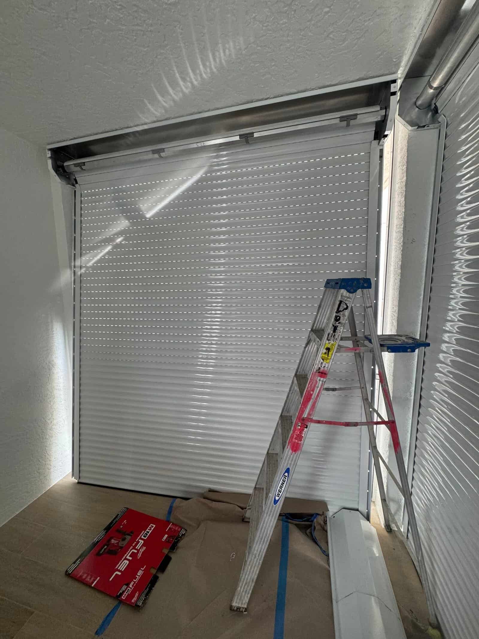 SAS Aluminum crew installing a roll-down hurricane shutter housing with ladder and tools on site in Southwest Florida