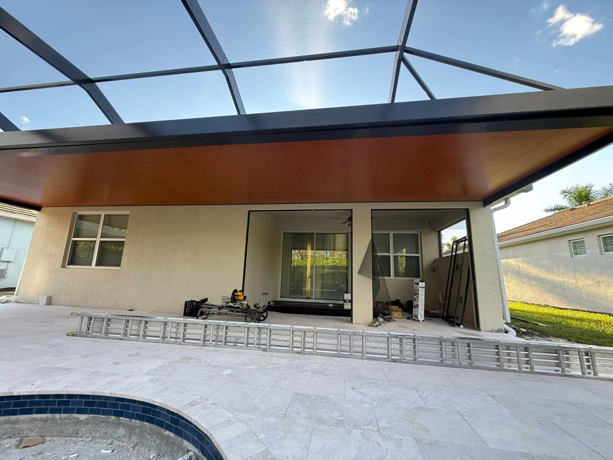 Upward view of wood-look covered lanai ceiling, dark aluminum framing and adjoining screened pool cage at Stillwater in Naples, Florida.