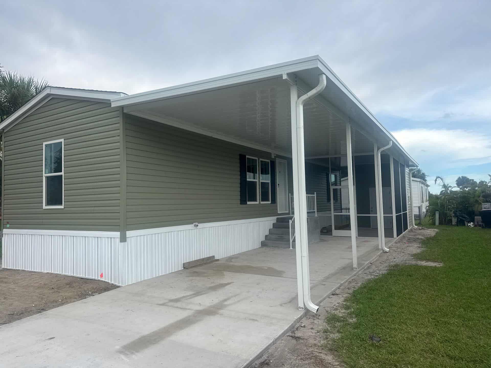 White aluminum pan-roof carport and screen room beside a manufactured home in Micco, Florida.