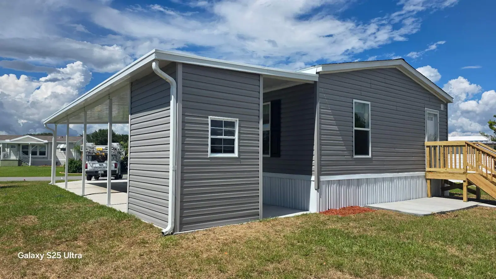 Gray-sided storage shed beneath the end of a white aluminum carport beside a manufactured home in Bradenton, Florida.